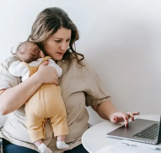 Selbstständige Mutter arbeitet am Laptop und hält ihr Baby im Arm