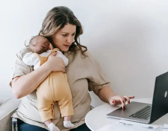 Selbstständige Mutter arbeitet am Laptop und hält ihr Baby im Arm