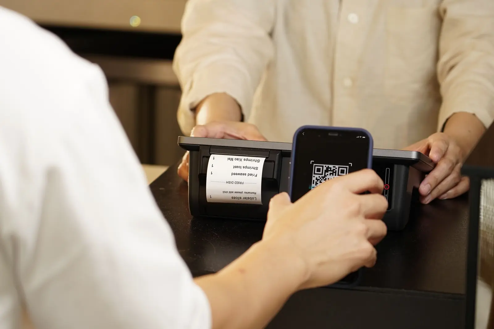 Person scannt einen QR-Code an einem Kassensystem mit einem Smartphone