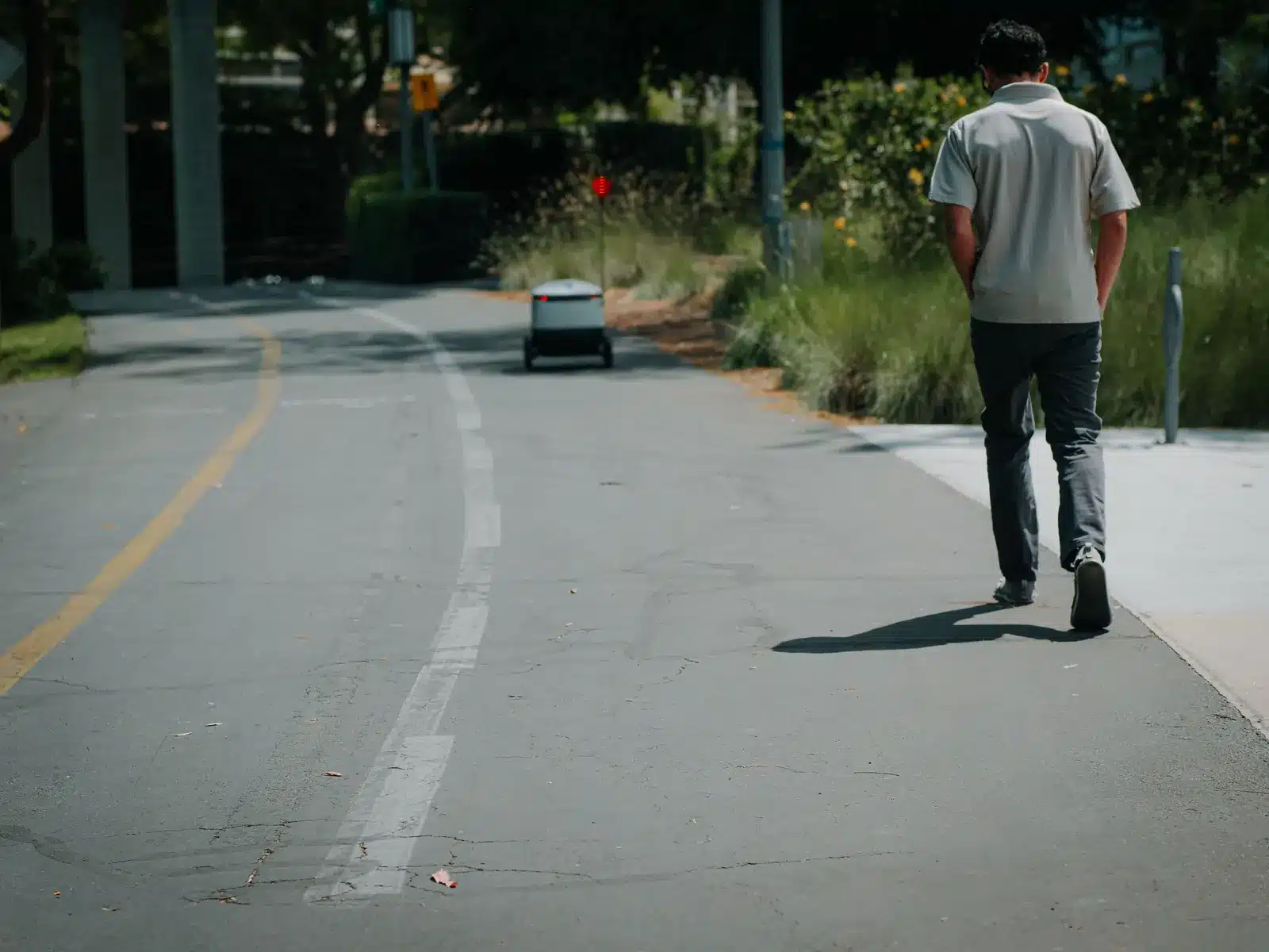Kleiner autonomer Lieferroboter fährt neben einem Fußgänger auf einer ruhigen Straße