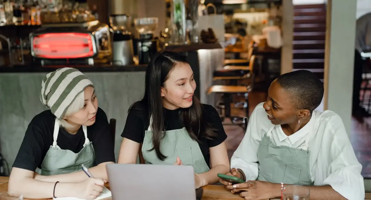 Drei Kolleginnen mit unterschiedlichem Hintergrund planen gemeinsam in einem Café