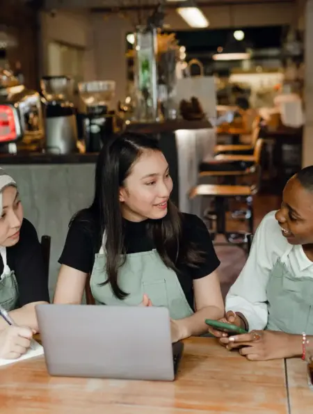 Drei Kolleginnen mit unterschiedlichem Hintergrund planen gemeinsam in einem Café
