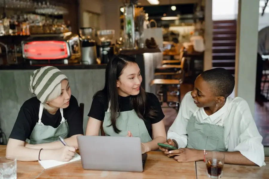 Drei Kolleginnen mit unterschiedlichem Hintergrund planen gemeinsam in einem Café
