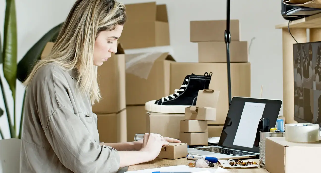 Unternehmerin verpackt Waren an einem Arbeitsplatz mit Laptop