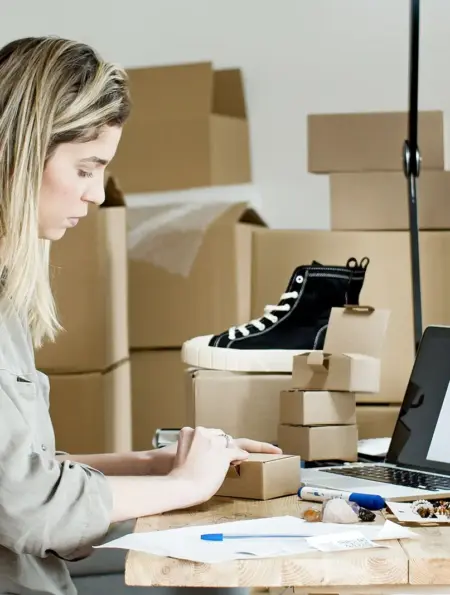Unternehmerin verpackt Waren an einem Arbeitsplatz mit Laptop