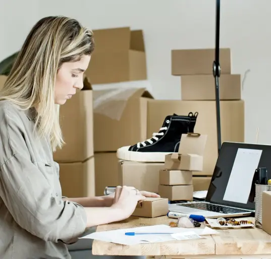 Unternehmerin verpackt Waren an einem Arbeitsplatz mit Laptop