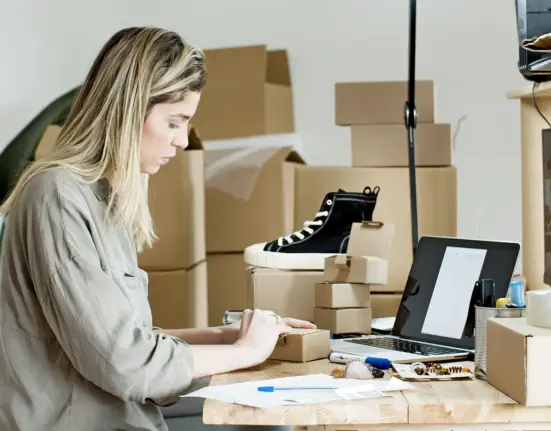 Unternehmerin verpackt Waren an einem Arbeitsplatz mit Laptop