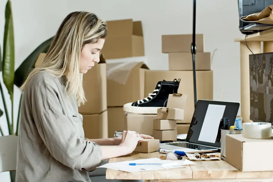 Unternehmerin verpackt Waren an einem Arbeitsplatz mit Laptop