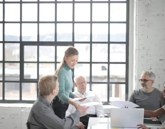 Älterer Mitarbeiter bespricht Unterlagen mit einem altersgemischten Team im Büro