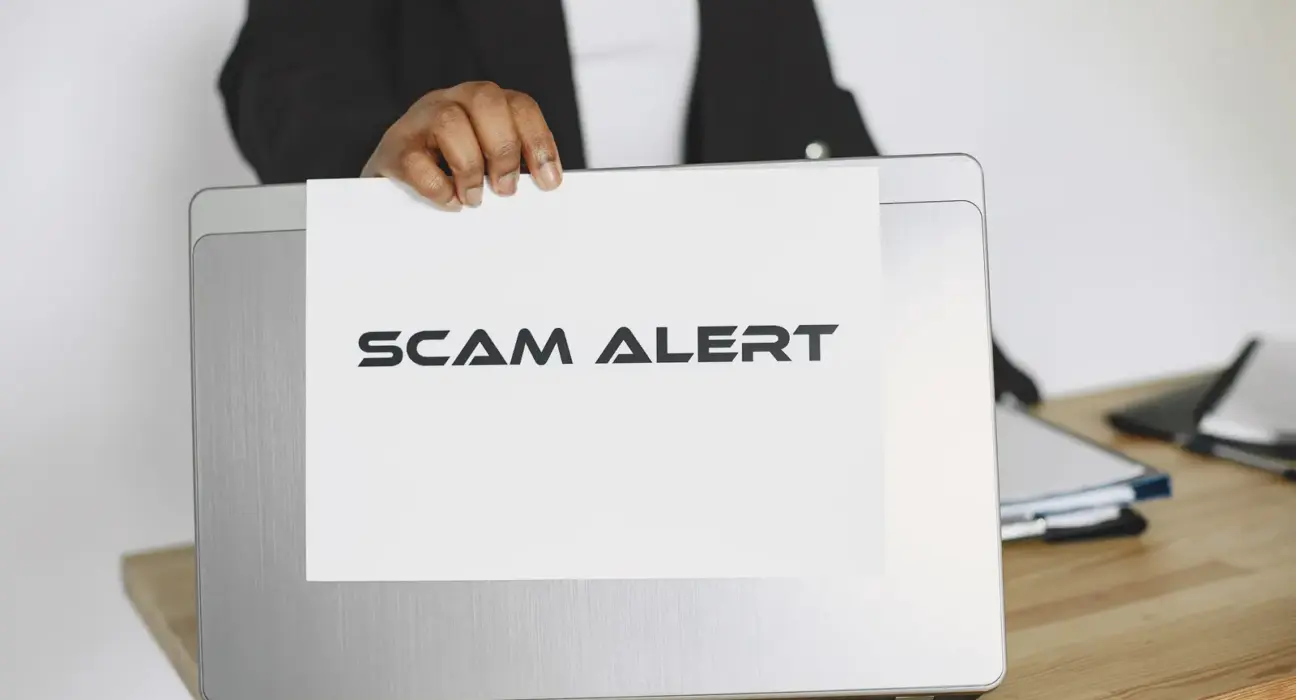 Geschäftsperson hält ein Schild mit der Aufschrift Scam Alert vor einen Laptop