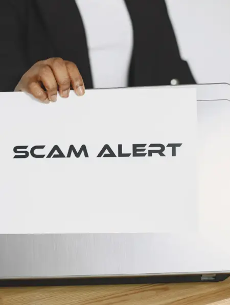Geschäftsperson hält ein Schild mit der Aufschrift Scam Alert vor einen Laptop