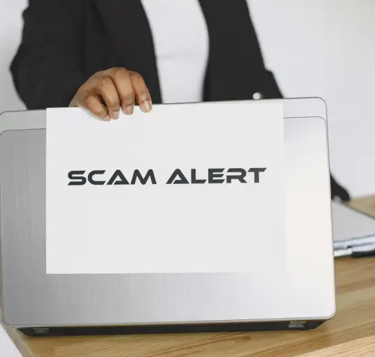 Geschäftsperson hält ein Schild mit der Aufschrift Scam Alert vor einen Laptop