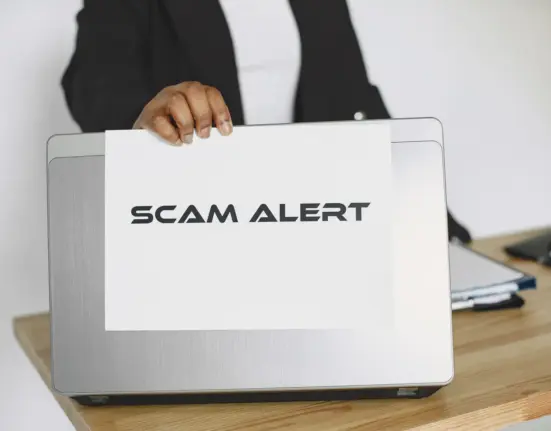 Geschäftsperson hält ein Schild mit der Aufschrift Scam Alert vor einen Laptop