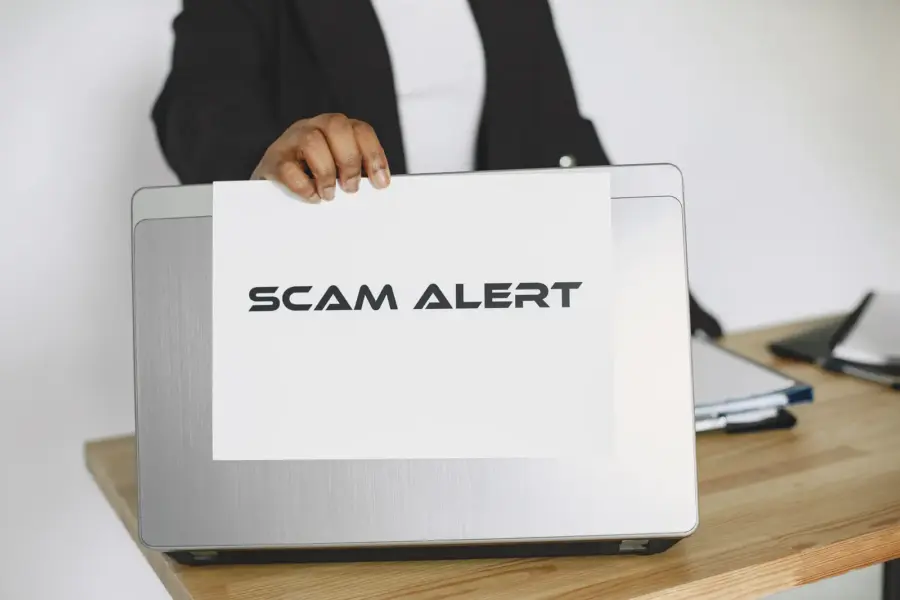 Geschäftsperson hält ein Schild mit der Aufschrift Scam Alert vor einen Laptop