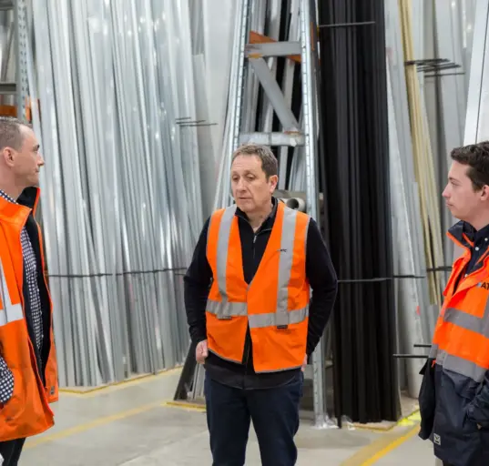 Drei Beschäftigte besprechen die Arbeitsplanung in einer Produktionshalle