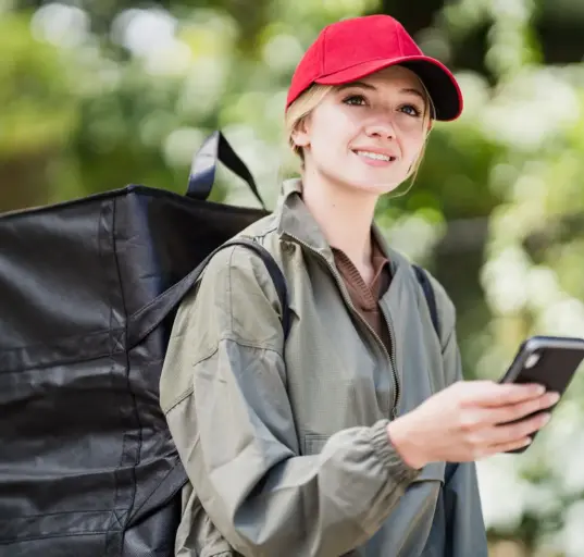 Kurierin mit Lieferucksack hält bei der Arbeit ein Smartphone in der Hand