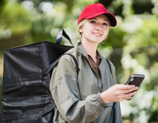Kurierin mit Lieferucksack hält bei der Arbeit ein Smartphone in der Hand
