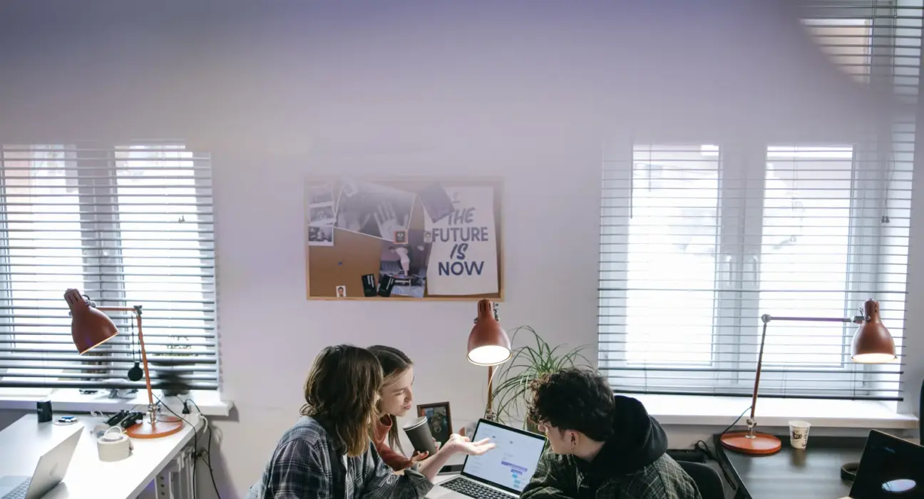 Drei Personen besprechen in einem hellen Büro die Umstellung mehrerer Arbeitsplatz-Laptops