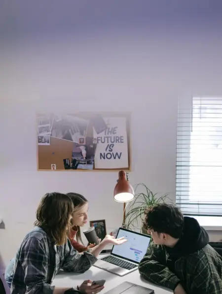 Drei Personen besprechen in einem hellen Büro die Umstellung mehrerer Arbeitsplatz-Laptops