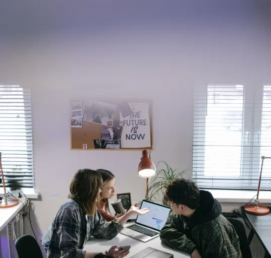 Drei Personen besprechen in einem hellen Büro die Umstellung mehrerer Arbeitsplatz-Laptops
