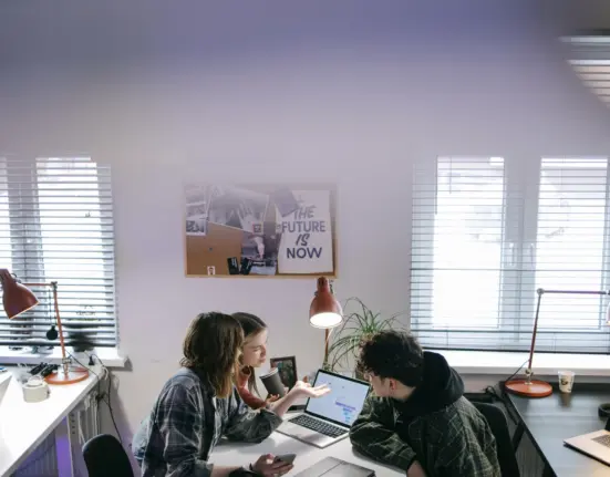 Drei Personen besprechen in einem hellen Büro die Umstellung mehrerer Arbeitsplatz-Laptops